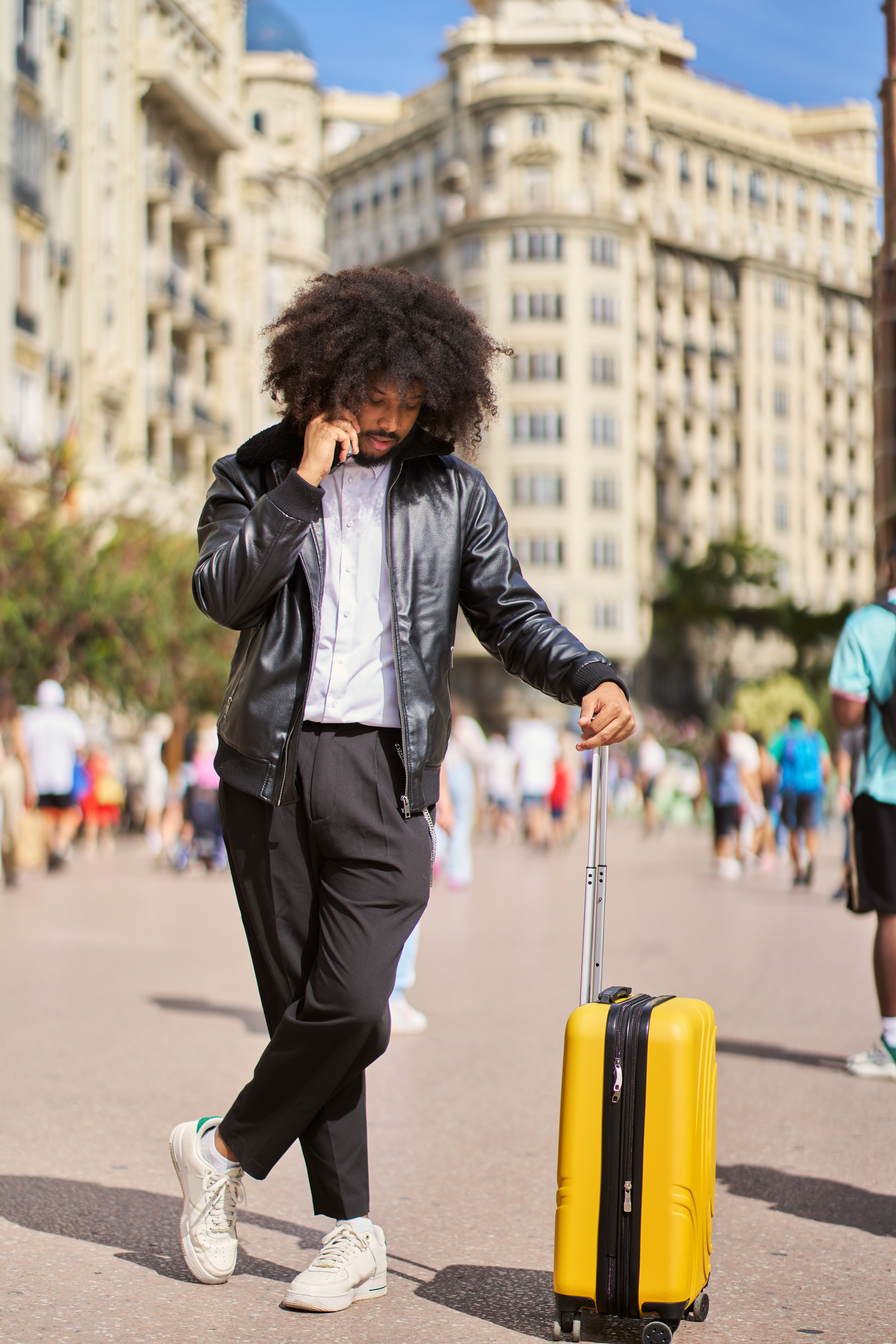 A young Black man walking through a city with his suitcase